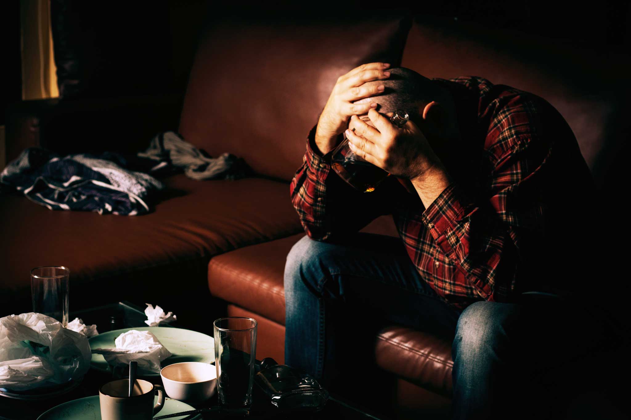 young man sitting on the couch struggling with the dangers of drinking and drug use