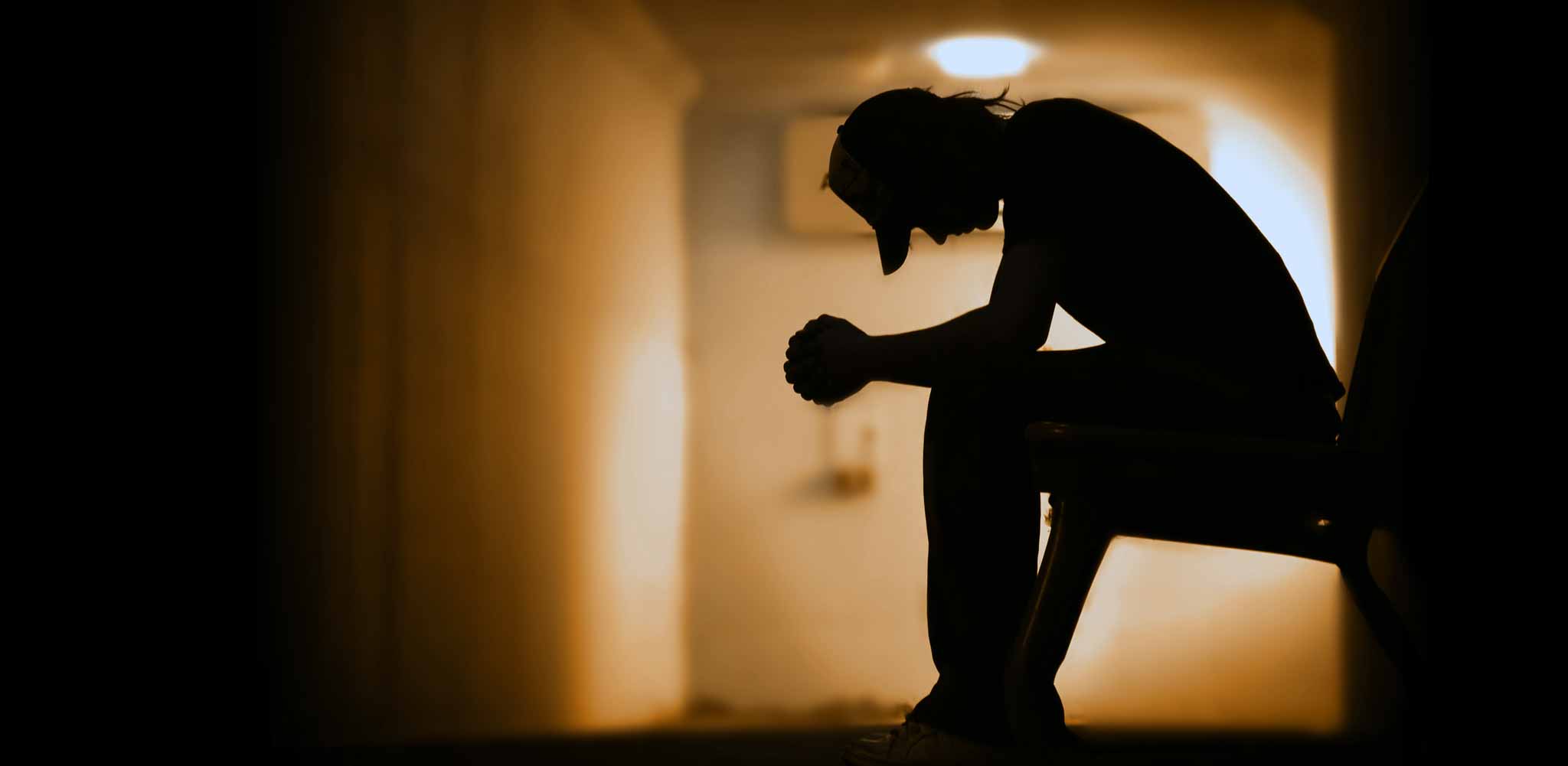 Silhouette of a young man sitting with his head down as he thinks about drug addiction among young adults