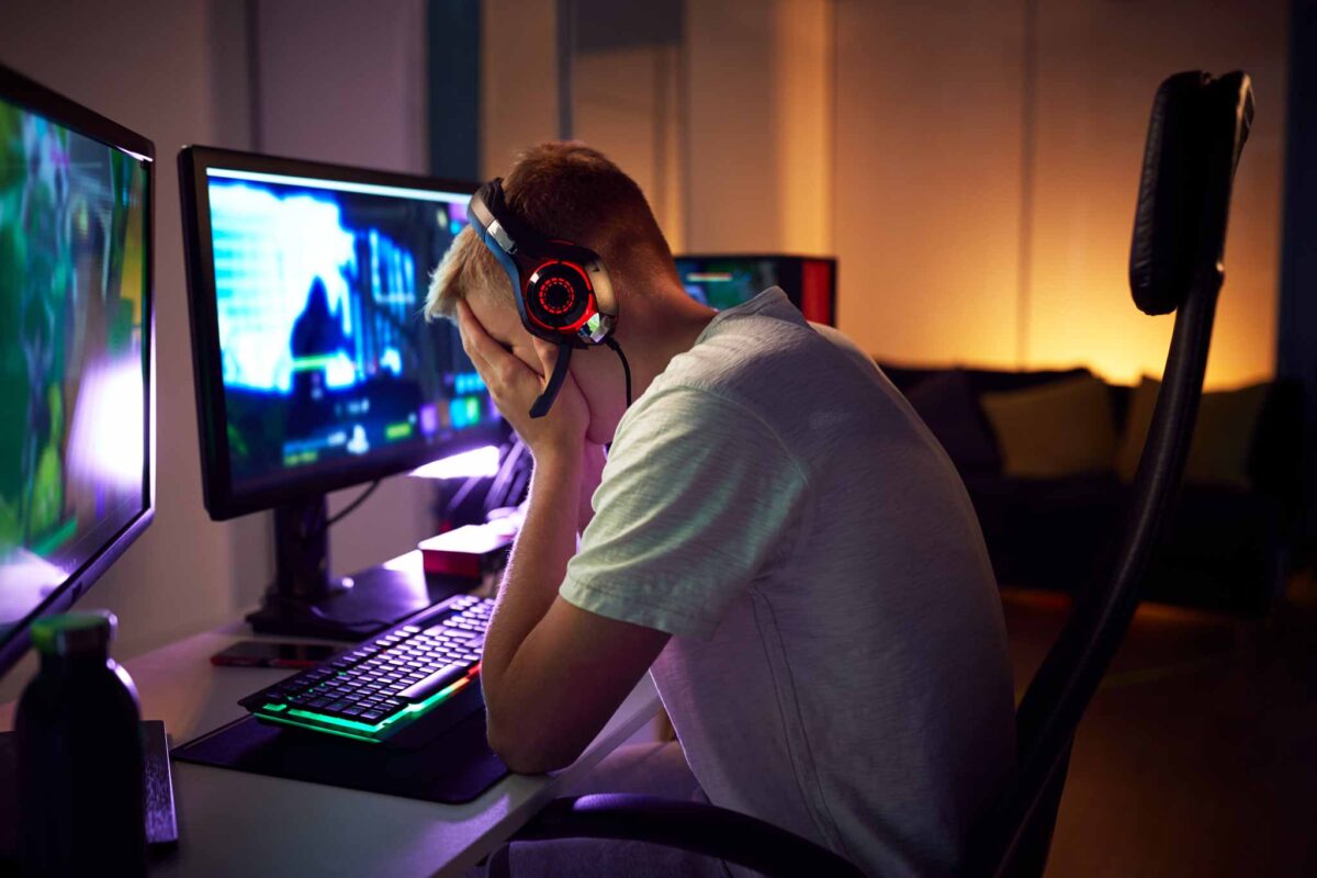 young man with his face in his hands in front of the computer showing emotional signs of social media addiction
