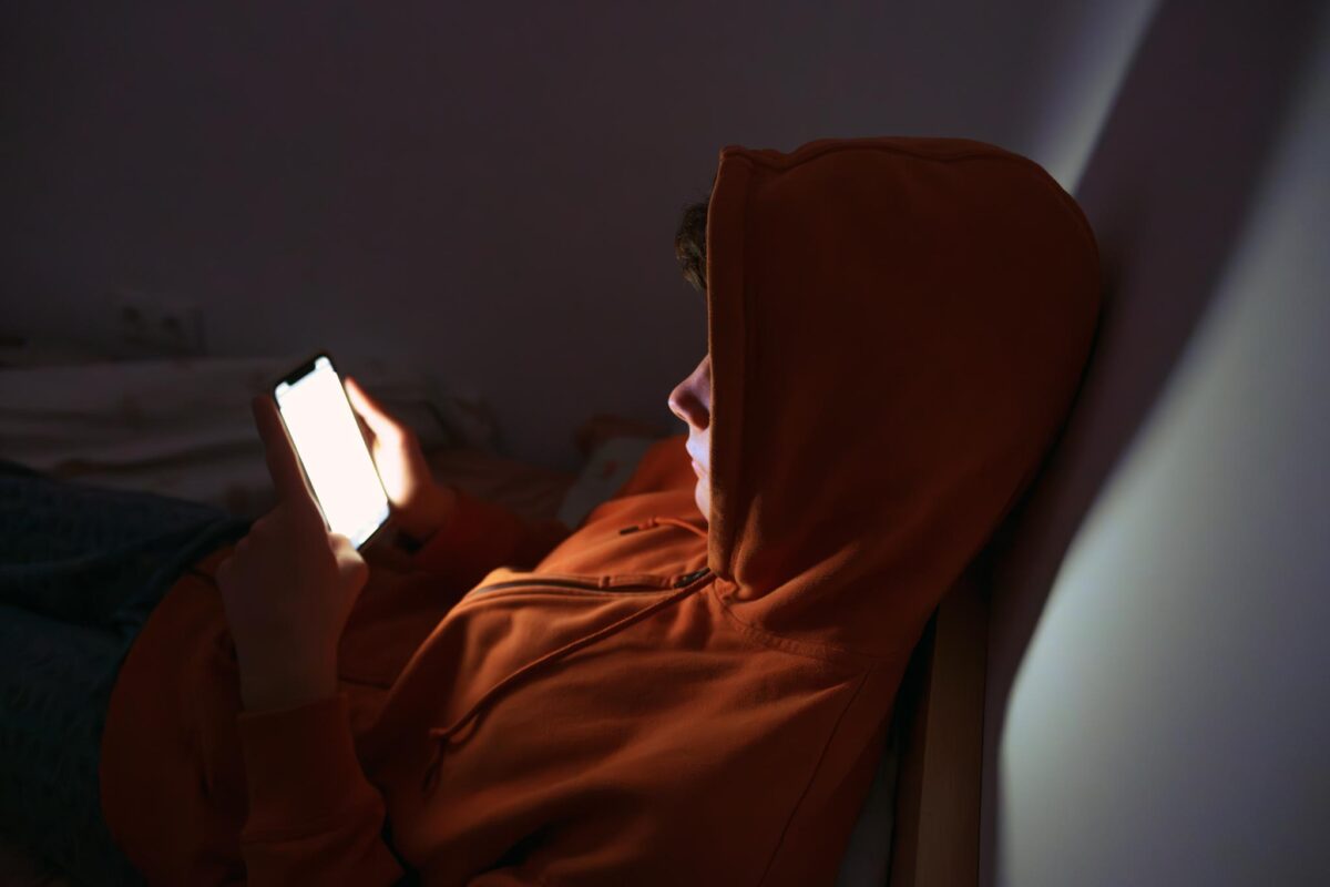 young man glued to his phone screen with his hood up showing behavioral signs of social media addiction